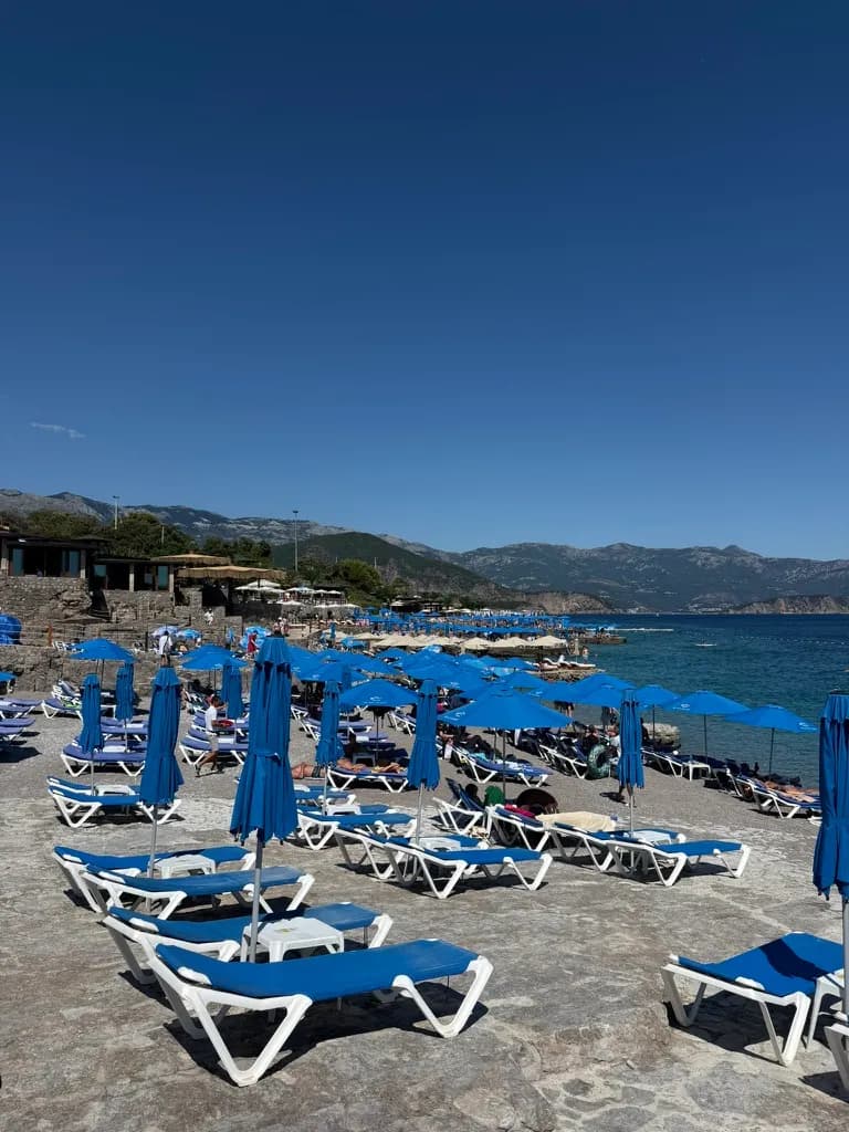 Leżaki i niebieskie parasole na brzegu plaży Ploče, ostatniego przystanku linii Budva – Jaz – Trsteno – Ploče.